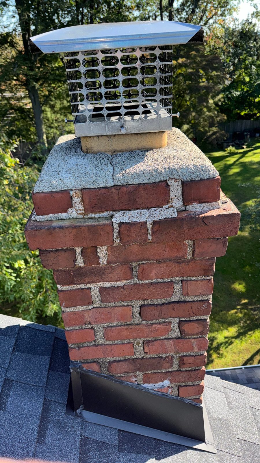 Brick chimney in Pompton Plains, NJ before repointing, with eroded mortar joints, a cracked crown and an old chimney cap