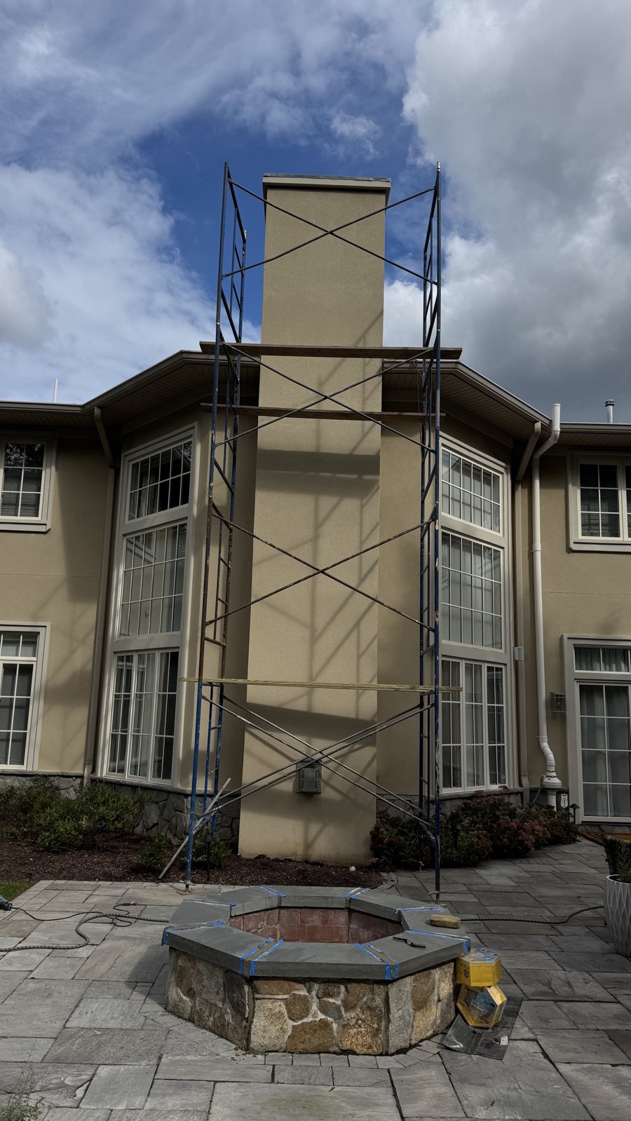 Scaffolding set up around a full-height stucco chimney on a home in Denville, NJ, with the patio and fire pit protected